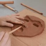 Mains d'enfants en train de travailler les détails d'un masque en argile avec un outil